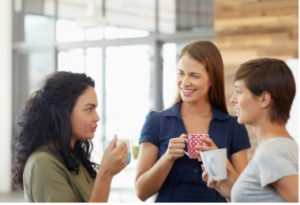 Du manque de communication au travail à l'aisance relationnelle - trois femmes qui discutent en prenant un café et en souriant, debout